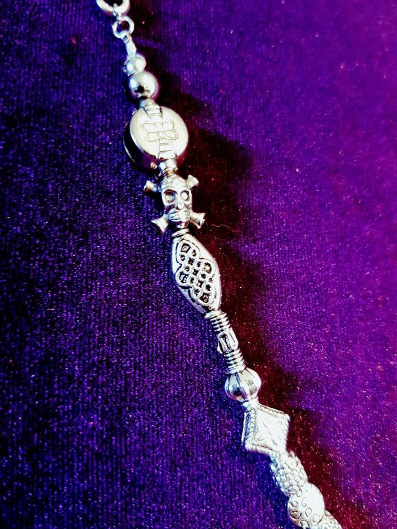 May include: A silver necklace with a skull charm, a decorative bead, and a snake charm. The necklace is on a purple background.