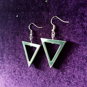 May include: A pair of silver triangle earrings with a hollow center. The earrings are hanging from a purple velvet background.