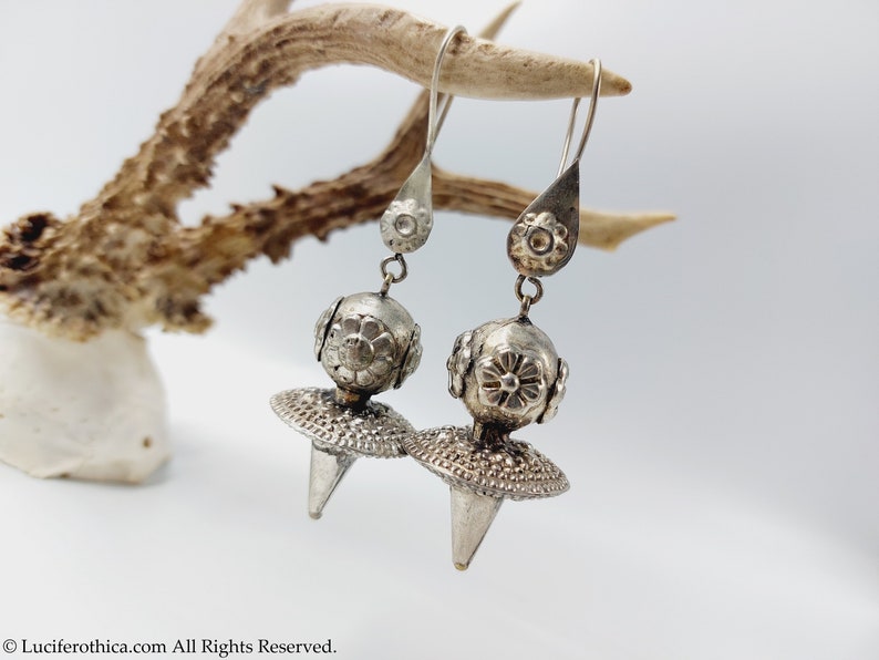 May include: A pair of silver dangle earrings with a round, floral-embossed bead and a pointed, textured disc.