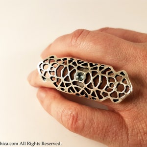 May include: A silver ring with a geometric design and a light blue gemstone. The ring is designed to be worn on the middle finger.