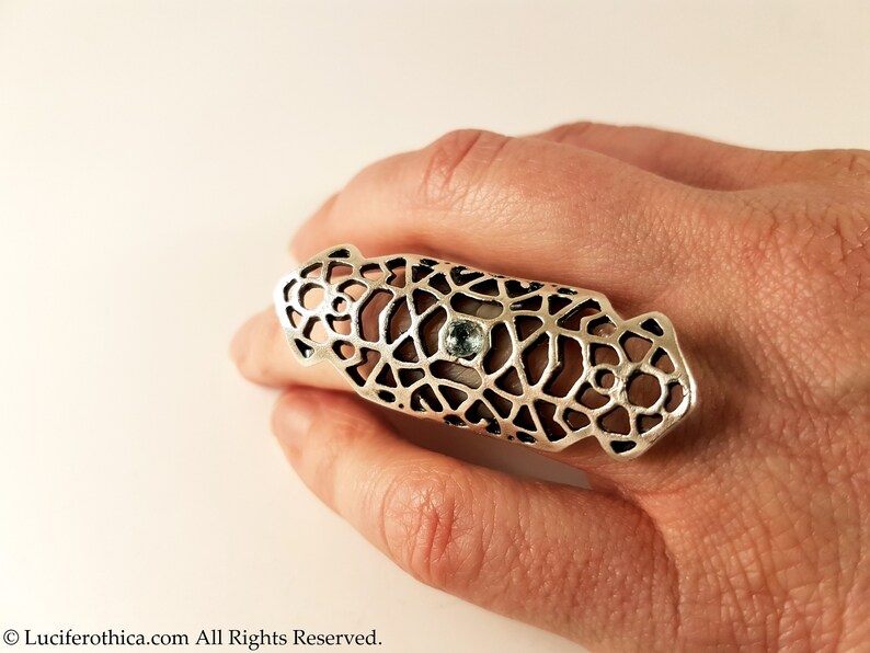 May include: A silver ring with a geometric design and a light blue gemstone. The ring is designed to be worn on the middle finger.
