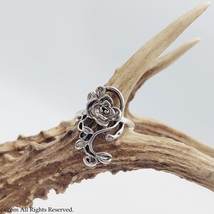 K&ouml;nnte beinhalten: Ein silberner Ring mit einem detaillierten Rosenmotiv. Die Rose ist aus filigraner, kunstvoller Metallarbeit gefertigt und auf einem schlichten Band befestigt.