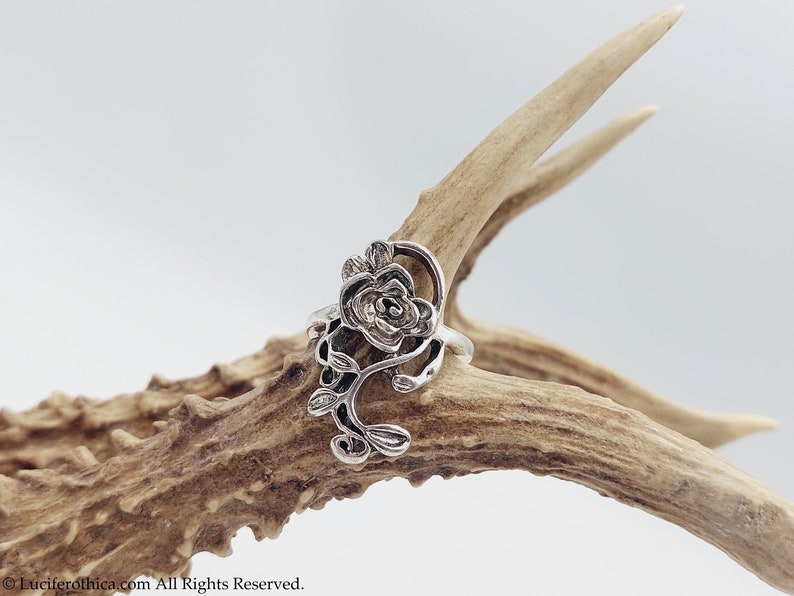 K&ouml;nnte beinhalten: Ein silberner Ring mit einem detaillierten Rosenmotiv. Die Rose ist aus filigraner, kunstvoller Metallarbeit gefertigt und auf einem schlichten Band befestigt.
