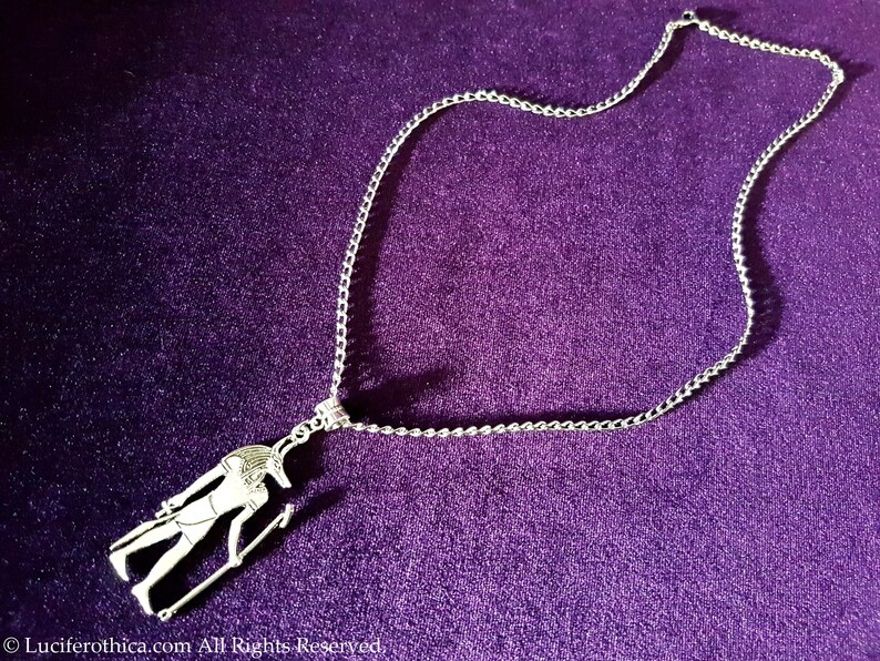 May include: Silver chain necklace with a pendant featuring an Egyptian god Anubis figure.