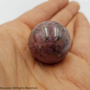 May include: A smooth, polished pink and grey sphere of rhodonite, a crystal known for its grounding and calming properties.
