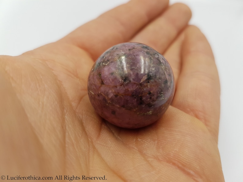 May include: A smooth, polished pink and grey sphere of rhodonite, a crystal known for its grounding and calming properties.