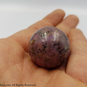 May include: A purple and black sphere-shaped crystal with a smooth, polished surface.