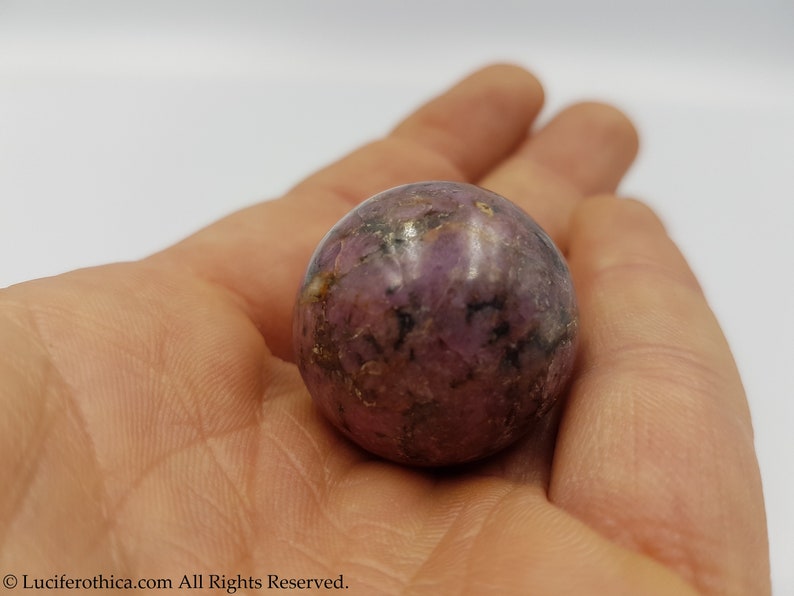 May include: A purple and black sphere-shaped crystal with a smooth, polished surface.