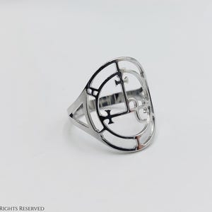 May include: A silver ring with a circular design featuring a cross and other geometric shapes.