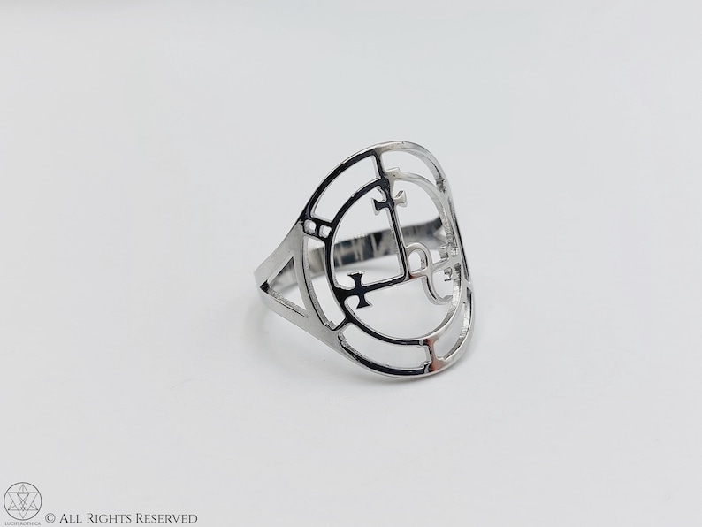 May include: A silver ring with a circular design featuring a cross and other geometric shapes.
