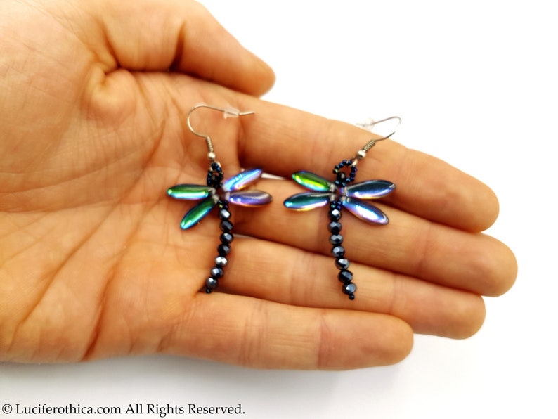 May include: A pair of iridescent dragonfly earrings with black bead accents. The earrings are dangle style and feature a silver hook.