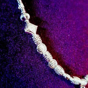 May include: A silver necklace with a variety of decorative beads and charms. The necklace is on a purple background.