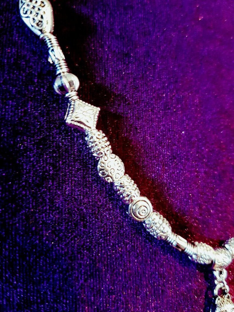 May include: A silver necklace with a variety of decorative beads and charms. The necklace is on a purple background.