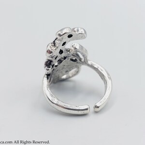 K&ouml;nnte beinhalten: Ein silberner Ring mit einem detaillierten Design, das einer stilisierten Hand mit mehreren Fingern &auml;hnelt. Der Ring ist offen und verstellbar.