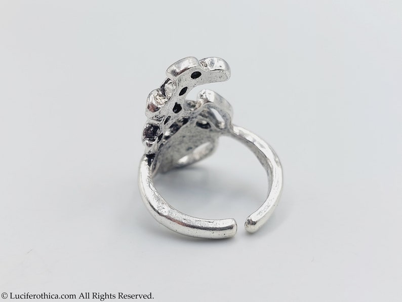 K&ouml;nnte beinhalten: Ein silberner Ring mit einem detaillierten Design, das einer stilisierten Hand mit mehreren Fingern &auml;hnelt. Der Ring ist offen und verstellbar.