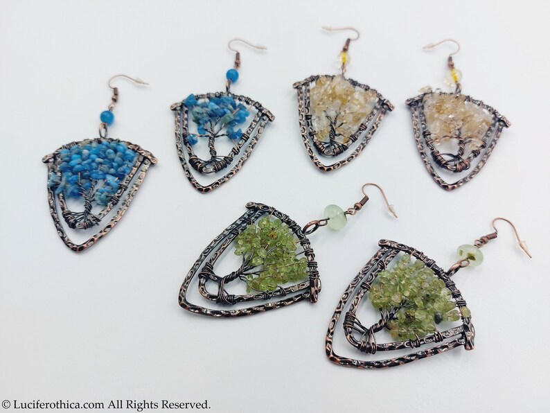 May include: A set of six copper wire tree of life earrings featuring different coloured gemstones. The earrings are shaped like a triangle with a tree design in the centre. The gemstones are blue, green and yellow.