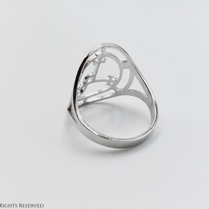 May include: A silver ring with a geometric design. The ring is open in the front and has a delicate, intricate pattern.