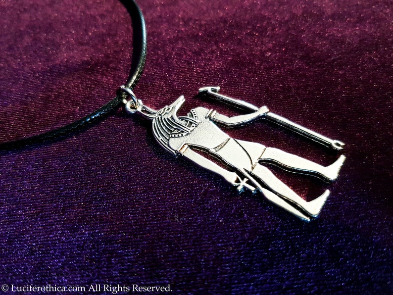 May include: Silver pendant necklace featuring an Anubis figure holding a staff. The pendant is on a black leather cord.