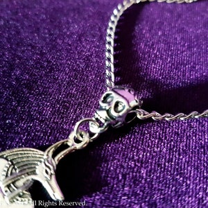 May include: A silver chain necklace with a skull charm and a detailed silver pendant. The necklace is on a purple background.