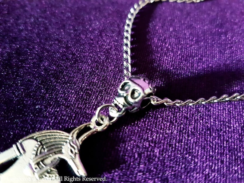 May include: A silver chain necklace with a skull charm and a detailed silver pendant. The necklace is on a purple background.
