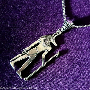 May include: Silver necklace featuring a pendant depicting an Egyptian god with a jackal head. The pendant is detailed and intricate, with the god holding a staff in one hand.