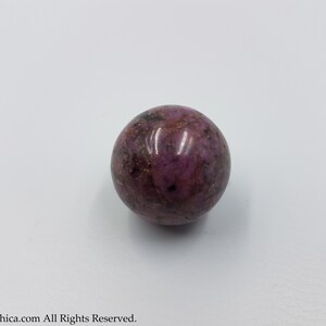 May include: A smooth, round, purple and pink sphere of polished rhodonite.