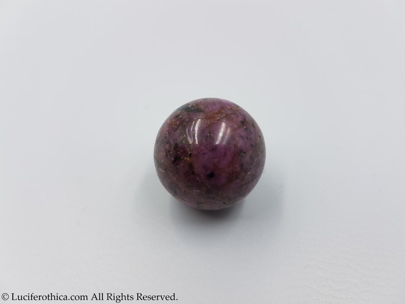 May include: A smooth, round, purple and pink sphere of polished rhodonite.