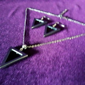 May include: A silver necklace and earrings set with black triangle pendants. The necklace has a delicate chain and a small silver bead at the top.