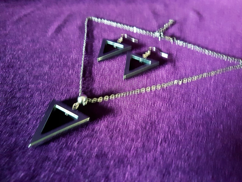 May include: A silver necklace and earrings set with black triangle pendants. The necklace has a delicate chain and a small silver bead at the top.