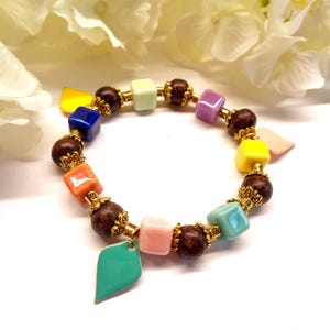Peut inclure: Un bracelet coloré composé de diverses perles. Il comprend des perles carrées multicolores, des perles rondes marron foncé et des détails dorés. Un charm en forme de feuille turquoise est suspendu au bracelet.