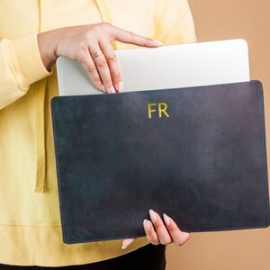 May include: A black leather laptop sleeve with gold lettering that says "FR".
