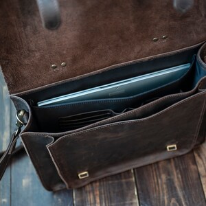 May include: A brown leather briefcase with a laptop inside. The briefcase has a flap that closes with a buckle and a shoulder strap.