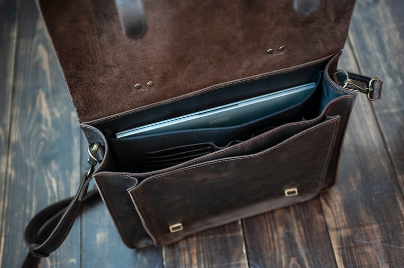 May include: A brown leather briefcase with a laptop inside. The briefcase has a flap that closes with a buckle and a shoulder strap.