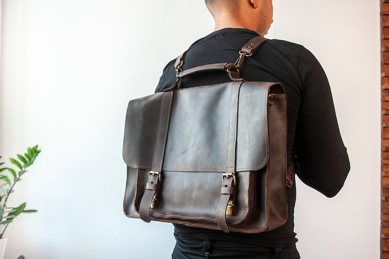 May include: A brown leather briefcase with a strap that can be worn as a backpack. The bag has two buckles and a flap.