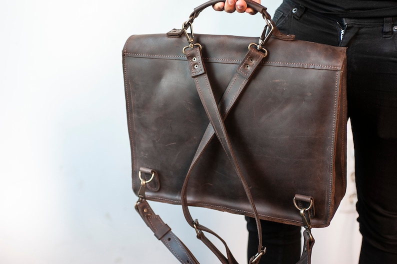 May include: A brown leather briefcase with adjustable straps that can be worn as a backpack. The briefcase has a top handle and metal hardware.