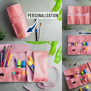 May include: A pink roll-up stationery organiser featuring multiple interior pockets and slots for pens, pencils, and office supplies. The exterior displays the text PERSONALISATION and the gold-coloured initials KS on the front flap.