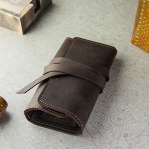 May include: A brown leather tobacco pouch with a strap closure. The pouch is rolled up and tied with the strap.