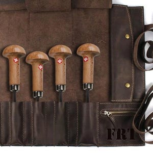 May include: A brown leather roll-up case with six slots for holding tools. The case has a zipper closure and a strap with a buckle. The case is rolled up and has the letters "FRT" printed on the front.