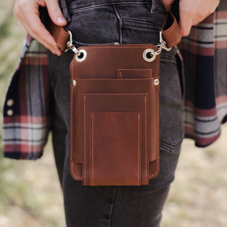 May include: A brown leather belt bag with multiple pockets and a silver buckle. The bag is worn on a person's hip.