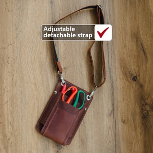 May include: A brown leather tool bag with an adjustable detachable strap. The bag has a pocket with a pair of scissors and a red tool inside.