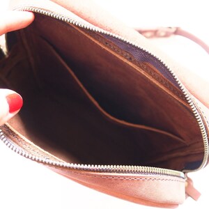 Puede incluir: El interior de un bolso de cuero marr&oacute;n con cierre de cremallera. El bolso tiene un peque&ntilde;o bolsillo en el interior.