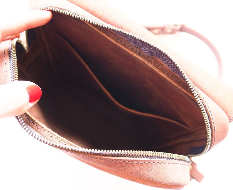 Puede incluir: El interior de un bolso de cuero marr&oacute;n con cierre de cremallera. El bolso tiene un peque&ntilde;o bolsillo en el interior.