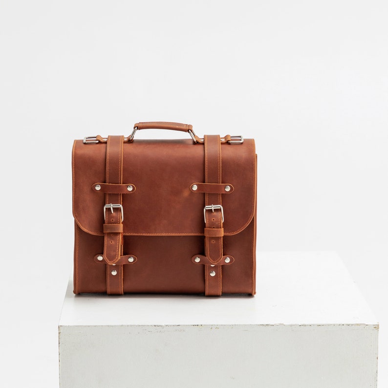 K&ouml;nnte beinhalten: Eine braune Ledertasche mit silbernen Schnallen und Metalldetails. Die Tasche hat einen oberen Griff und einen Klappverschluss.