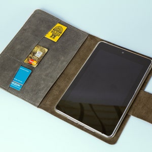 Op de afbeelding: Een bruine leren tablet-hoes met een flap die over het scherm vouwt. De hoes heeft meerdere kaartsleuven aan de binnenkant en een flap die met een drukknoop sluit. De hoes is open en een tablet zit er in.