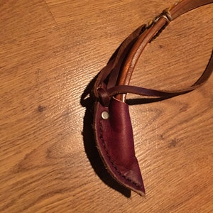 May include: A brown leather sheath with a metal button closure. The sheath is designed to hold a small knife or other tool.