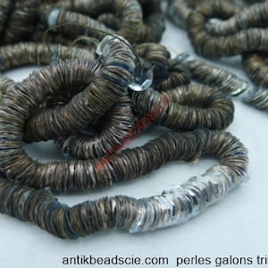 Peut inclure: Gros plan sur une garniture métallique enroulée, dans des tons de marron et d'argent. La garniture semble être composée de petits éléments circulaires, créant un effet texturé et superposé. La garniture est disposée en spirales lâches.