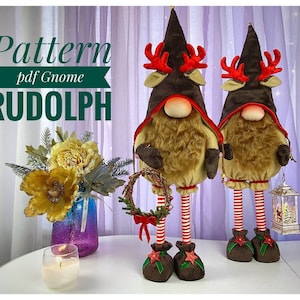 Op de afbeelding: Twee decoratieve kerstkabouters met bruine hoeden en rendiergeweien. De kabouters hebben lange, gestreepte benen en bruine laarzen. Eén kabouter houdt een kleine krans vast. De afbeelding bevat de tekst "Pattern pdf Gnome RUDOLPH".
