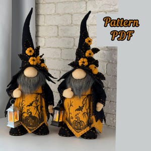 May include: Two fabric gnome dolls featuring tall black pointed hats decorated with small orange pumpkins. The gnomes wear orange tunics with black pumpkin and bat illustrations, grey beards, and hold small lanterns. Text reads Pattern PDF.