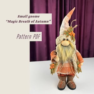 以下が含まれることがあります： オレンジとクリーム色のチェック柄の帽子と衣装を着た、手作りのノーム人形。ノームは長い黄色のひげを持ち、造花の実と葉で飾られています。画像には「Small gnome Magic Breath of Autumn Pattern PDF」と書かれています。