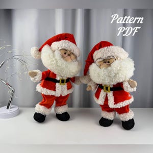 May include: Two Santa Claus plush dolls. Each doll wears a red suit with white trim, a black belt with a gold buckle, and a matching hat. They have round glasses and fluffy white beards. The text "Pattern PDF" is in the upper right corner.
